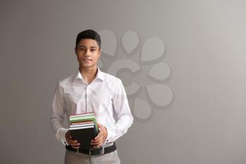 African-American schoolboy with books on grey background�