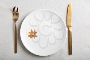 Plate with hashtag symbol and golden cutlery on light table�