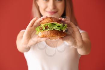 Beautiful young woman with tasty burger on color background, closeup�