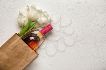 Bag with bottle of wine and flowers on white background�