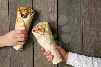 Female hands with tasty doner kebab on wooden background�