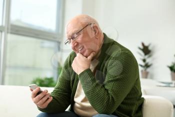 Senior man with hearing aid using mobile phone at home�