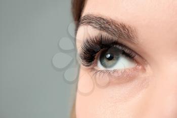 Young woman with beautiful eyelashes on grey background, closeup�