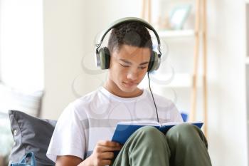 African-American teenage boy reading book at home�