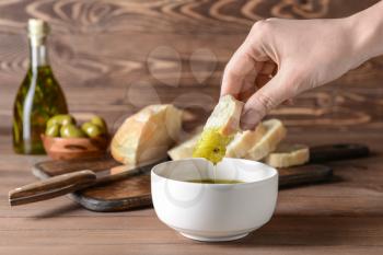Woman dipping fresh bread into tasty olive oil in bowl�