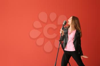 Teenage girl with microphone singing against color background�