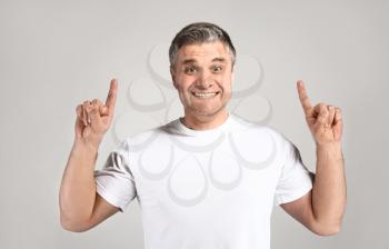 Handsome mature man with raised index fingers on grey background�