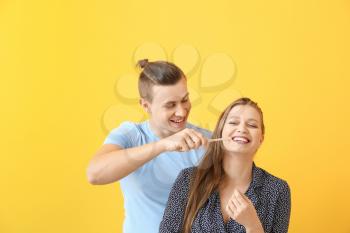 Happy man helping his girlfriend to clean teeth against color background�