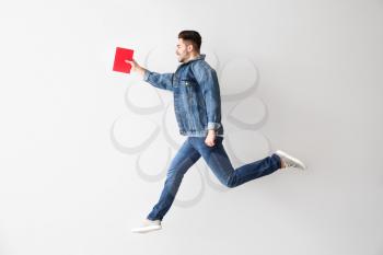 Jumping young man with book on light background�