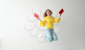 Jumping young woman with books on light background�