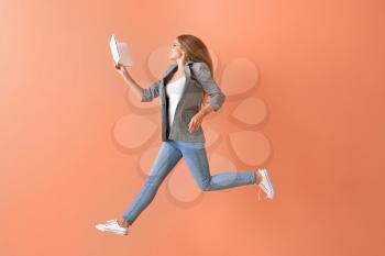 Jumping young woman with book on color background�