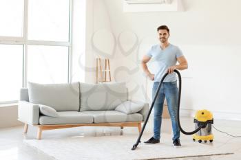Young man hoovering carpet at home�
