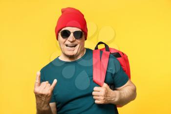 Portrait of stylish senior man showing devil horns gesture on color background�