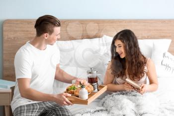 Young woman receiving breakfast in bed from her beloved husband�