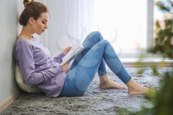 Beautiful young woman reading book at home�
