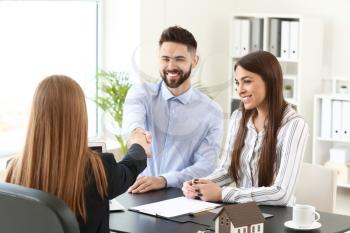 Real estate agent shaking hands with young couple in office�