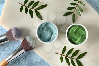 Bowls with cosmetic clays and brushes on color background�