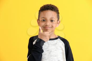 Cute African-American boy showing thumb-up on color background�