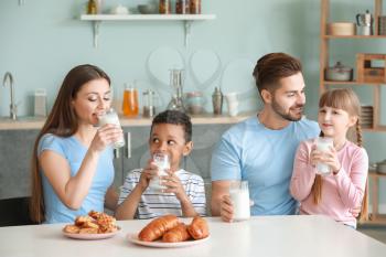 Young family drinking tasty milk in kitchen at home�