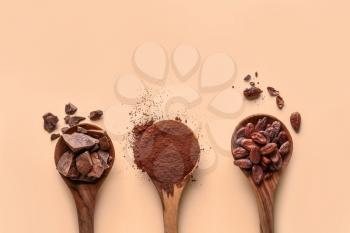 Spoons with cocoa powder, beans and chocolate on light background�