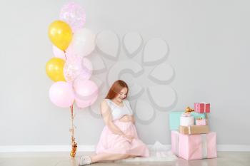 Beautiful pregnant woman with baby shower gifts near light wall�
