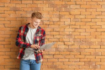 Handsome young man with laptop near brick wall�