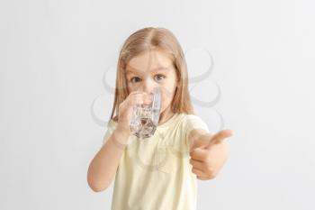 Cute little girl drinking water on light background�