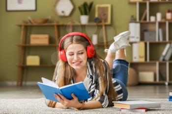Young woman listening to music and reading book at home�