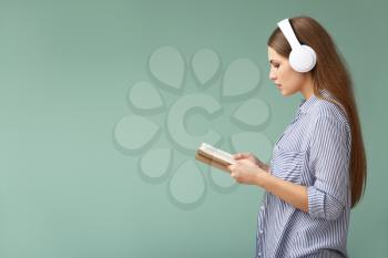 Young woman listening to music and reading book on color background�