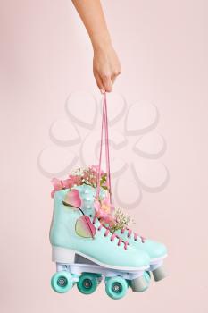 Woman holding vintage roller skates with flowers and sunglasses on light background�