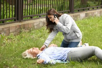 Female passer-by calling an ambulance for unconscious mature woman outdoors�