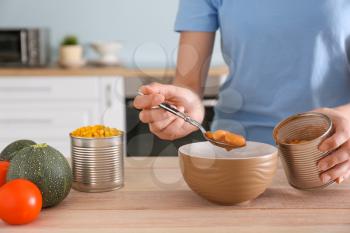 Woman taking beans from tin can at table in kitchen�