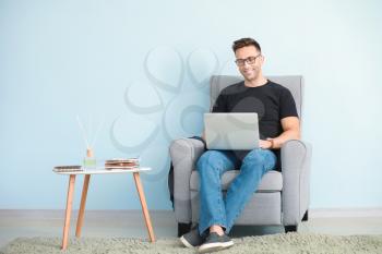 Male blogger with laptop sitting in armchair near color wall�