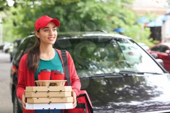 Female worker of food delivery service near car outdoors�