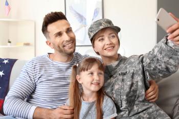 Happy female soldier taking selfie with her family at home�