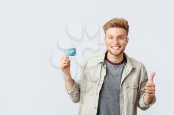 Happy young man with credit card showing thumb-up gesture on white background�