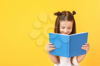 Cute little girl with book on color background�