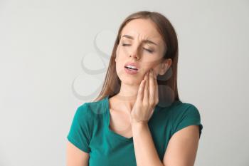 Young woman suffering from toothache against light background�