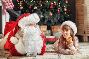 Santa Claus and little girl with cookie in room decorated for Christmas�