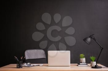 Stylish workplace with modern laptop near dark wall�