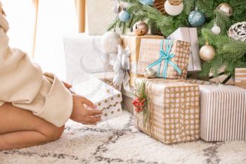 Woman putting gift boxes under Christmas tree�