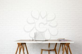 Table with modern laptop and chair near white brick wall�