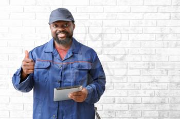 African-American car mechanic with tablet computer showing thumb-up near brick wall�