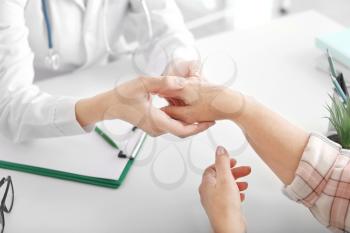 Doctor examining mature woman with joint pain in clinic, closeup�