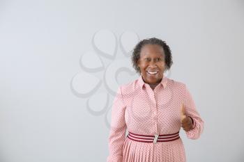 Portrait of African-American woman showing thumb-up on light background�