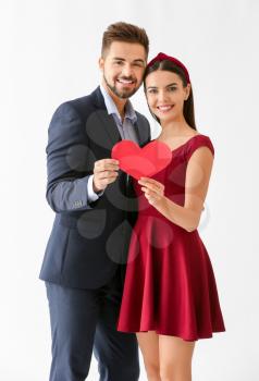 Portrait of beautiful young couple with paper heart on white background�
