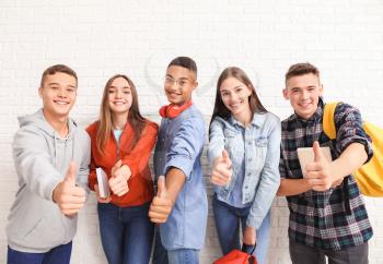 Portrait of teenagers showing thumb-up near white brick wall�