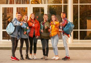 Group of teenage students showing thumb-up near university�