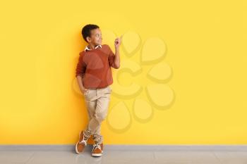 Fashionable African-American boy in autumn clothes pointing at something while standing near color wall�