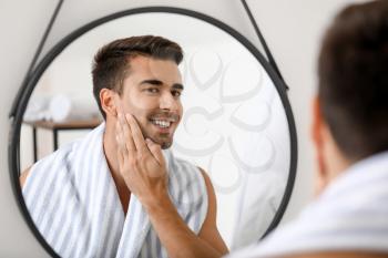 Handsome young man looking in mirror after shaving at home�